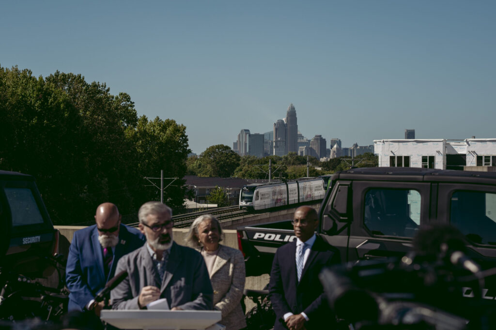 A train passes by as CATS interim CEO Brent Cagle addresses recent safety concerns, with Davidson Mayor Rusty Knox, Charlotte Mayor Vi Lyles, and city manager Marcus Jones behind him. Photo by Logan Cyrus