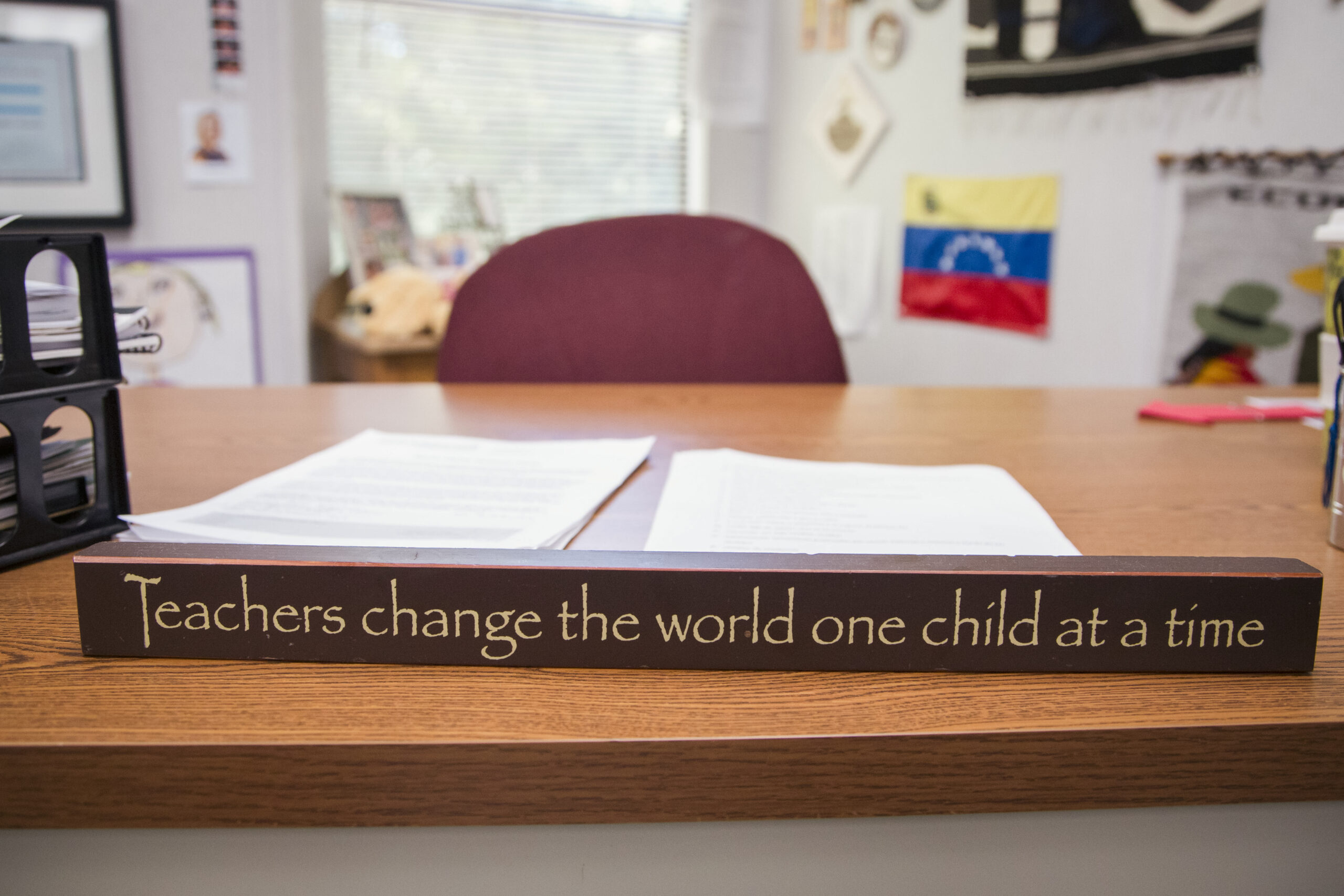 An empty teacher's desk with a wooden sign that reads "Teachers change the world one child at a time."